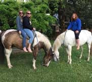 Two guests posing with horses on the green lawn of the homeplace